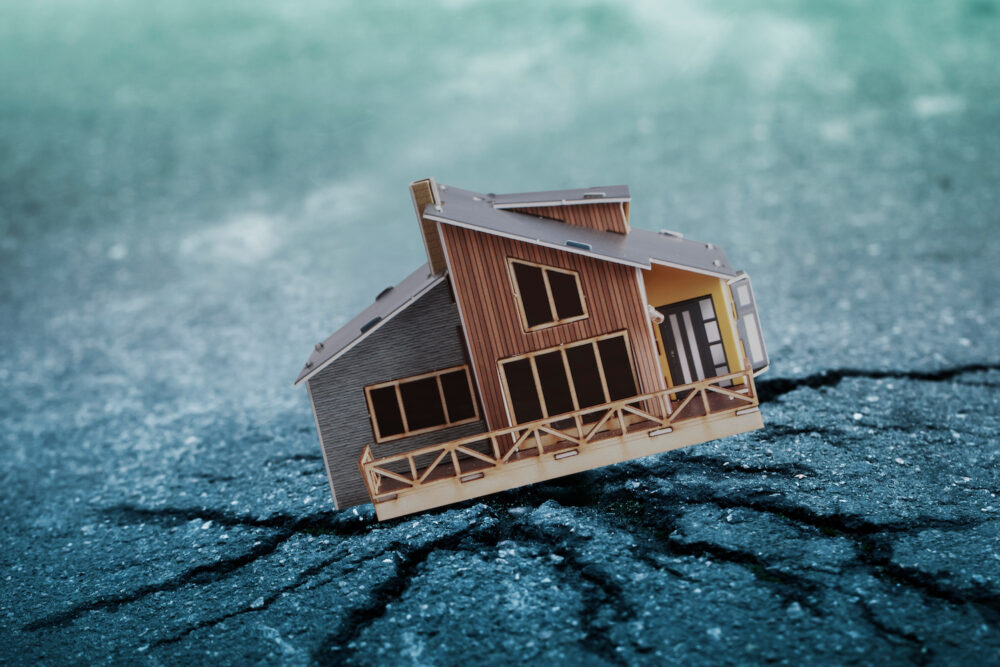 A small brown wooden model of a house sits on cracked concrete